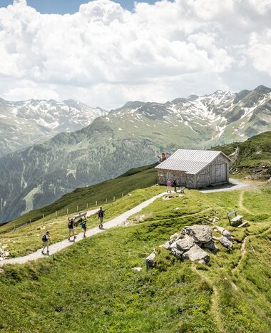 Group of hikers on mountain trail near wooden hut with view of snow-covered peaks in Gastein | © Gasteinertal Tourismus GmbH